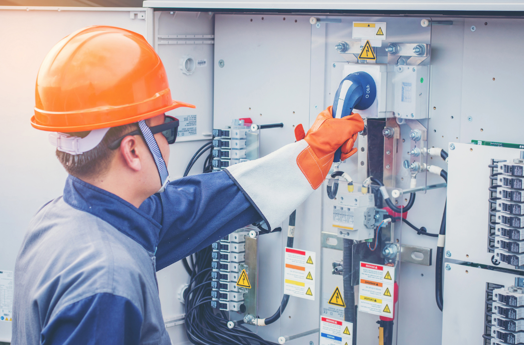 Eletricista executando manobra em quadro elétrico com proteções, disjuntores e cabeamento